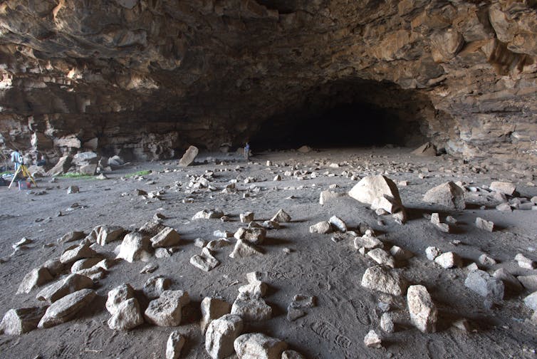 A photo of a rocky floor leading to a dark cave mouth, covered with rocks – some of which are roughly semicircular in shape.