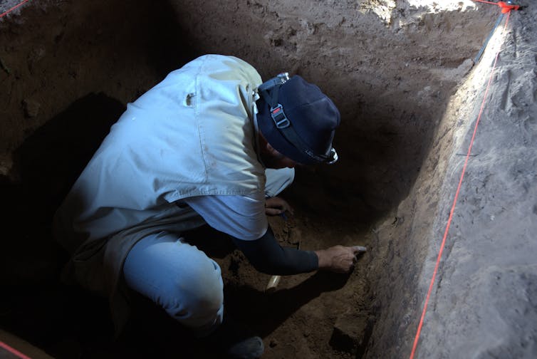 A photo of a man crouching in a pit, digging.