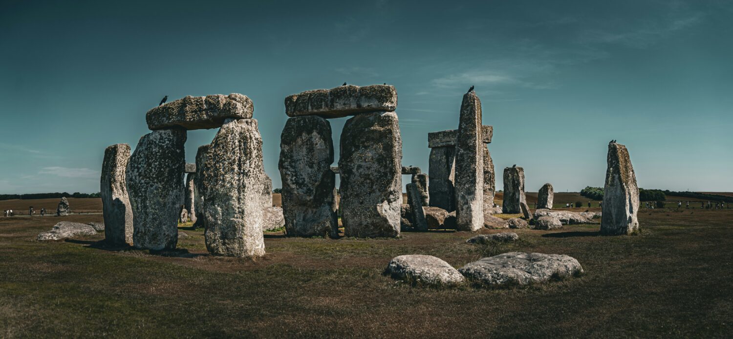 Standing stones at Stonehenge with crows on top. Small people are in the distance, giving a sense of scale.