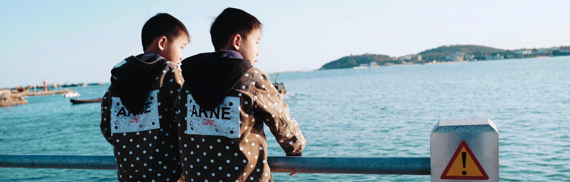 Twin boys dress alike stand looking out over the water.