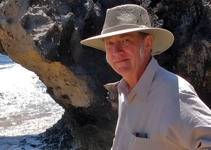 Professor Matt Cartmill wearing a hat and outdoor clothing standing in front of a large rock formation.