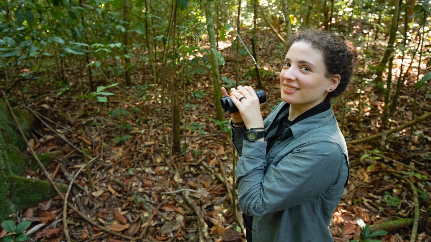 A scientist in the forest with binoculars.