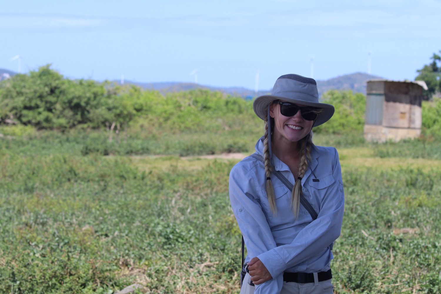 Brooklynn Scott in a blue shirt and hat, standing outside with a green background of low-growing plants.