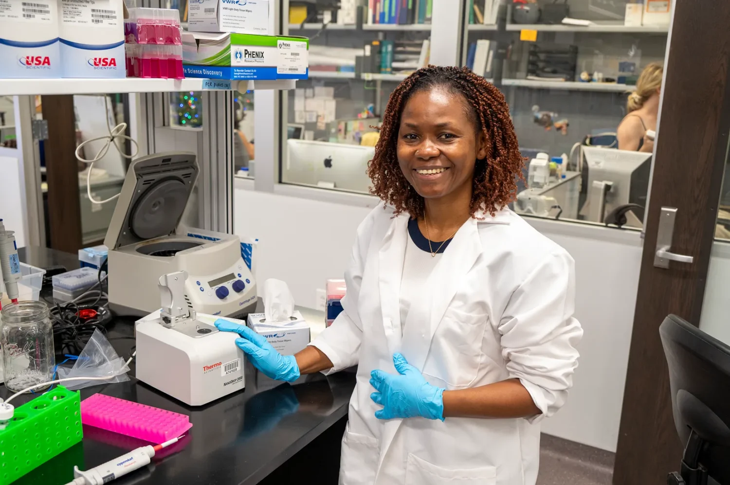 Florence Aghomo in a high tech lab wearing a white lab coat.